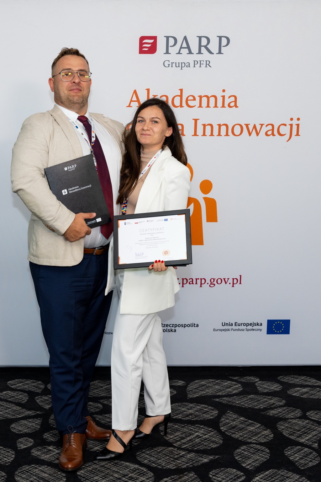 Uczestnicy z certyfikatem na tle Akademii Menadżera Innowacji PARP